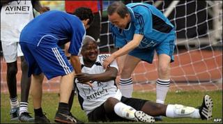 Uganda"s President, Yoweri Museveni (C) is helped to his feet by UN Secretary General, Ban Ki-moon, during a football match in Kampala
