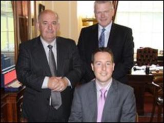 Mr Paul Givan (seated) with Speaker William Hay and the Director General Trevor Reaney after signing the Roll of Members