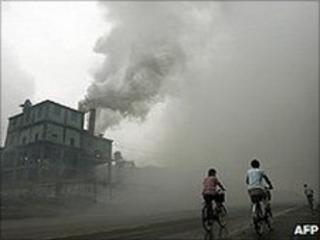 People cycling past a factory (Image: AFP)