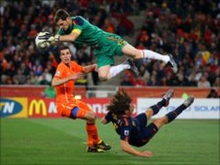 Iker Casillas of Spain catches the ball ahead of Robin Van Persie of the Netherlands as Carles Puyol of Spain falls to the ground during the World Cup final