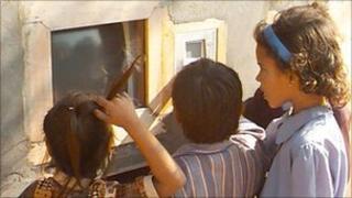 Children using computer via a hole in a wall