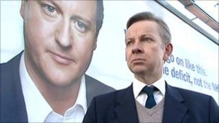 Michael Gove walking past campaign poster of David Cameron