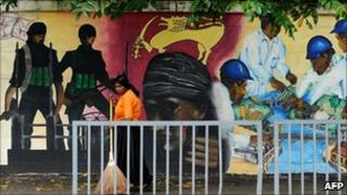 A Sri Lankan street cleaner sweeps the pavement alongside a mural in Colombo depicting the victory over Tamil Tiger rebels