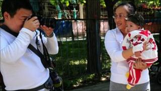 Отец фотографирует свою девочку, которую держат на руках у матери в парке в Пекине