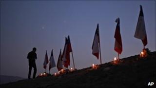 A man stands next to to Chilean flags representing 33 trapped miners outside the San Jose mine in Copiapo, Chile