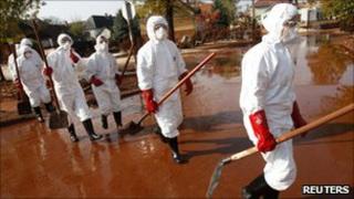 Volunteers in protective clothing walking through red mud in the flooded village of Devecser, Hungary