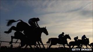 Horses jumping over a hurdle at sunset
