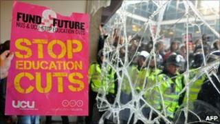 A Demonstrator holds a placard next to a broken window at 30 Millbank