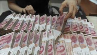 Chinese bank teller handling piles of yuan notes