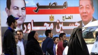 People in Cairo walk in front of election poster featuring President Hosni Mubarak (left) and a ruling NDP candidate