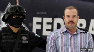 Drugs suspect Carlos Montemayor in chains, guarded by a masked police officer