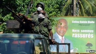 Presidential guard soldiers pass in front of a poster featuring Guinean presidential candidate Cellou Dalein Diallo on 2 December 2010 in Conakry