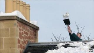 A man uses a shovel to remove snow from the roof of a house in Edinbu