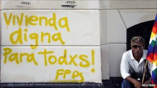 man holds a Wiphala indigenous flag next to graffiti calling for decent housing for all during a demonstration to demand housing for homeless people outside Buenos Aires City Hall on 14 December, 2010