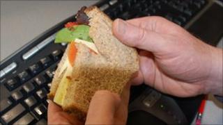 Man holding sandwich over computer keyboard
