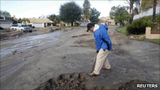 A man attempts to clear mud from his driveway in Highland, California