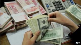 A bank teller counting stacks of US dollars and Chinese Yuan notes