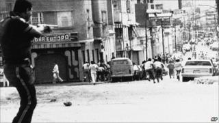 A policeman shoots a shotgun to a crowd in a neighborhood to prevent lootings and sackings by people protesting rises in transport fares in Caracas, Venezuela on 28 February 1989