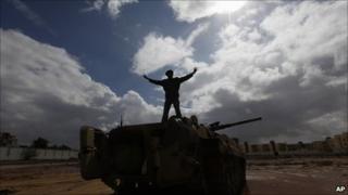 A Libyan man stands over a destroyed tank flashing a V signal, Al-Katiba military base, Benghazi, 24 February 2011
