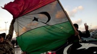 Libyan men hold the former royal flag as they drive past a demonstration against Libyan leader Muammar Gaddafi in Benghazi, eastern Libya, 27 February 2011