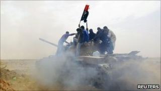 Rebels ride on a tank on the road leading to Brega