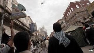 Anti-government protestors react as a military helocopter flies overhead during clashes in Sanaa, March 18, 2011