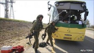 Israeli soldiers run past a bus hit by a mortar, southern Israel (7 April 2011)