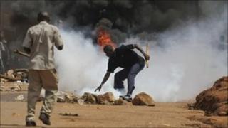 A Ugandan protester reaches down to pick up a tear gas grenade that police fired at a crowd in Kampala - 18 April 2011
