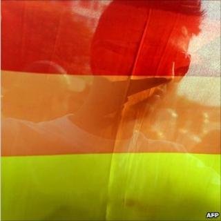 A man is seen behind a gay pride rainbow flag