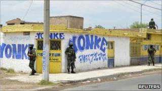 Soldiers stand guard outside a car junkyard neighbouring a vacant lot where a mass grave was found on 10 May, 2011