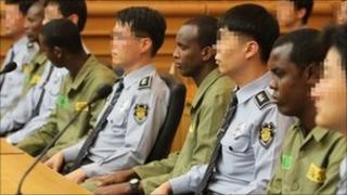 Somali pirates wearing green prison uniforms sit together with South Korean security guards as hearings begin at a court in the southern port city of Busan