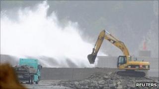 An excavator is seen as waves hit a temporary breakwater at a port that was devastated by the 11 March quake and tsunami in Miyako, Iwate prefecture