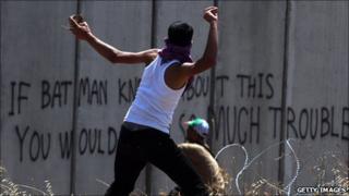 A Palestinian youth throws a stone towards Israeli soldiers standing on the other side of Israel's separation wall 3 June 2011.