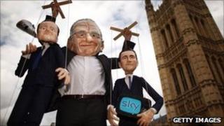 Puppets representing Prime Minister David Cameron (L) and Culture Secretary Jeremy Hunt (R) are held aloft by a protester dressed as Rupert Murdoch