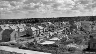 Облака собираются над длинными рядами одинаковых домов в строящемся имении. Он строится различными небольшими строительными фирмами, каждая из которых строит несколько домов., 1947