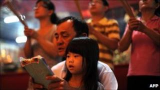 An ethnic Chinese family prays in front of a giant paper-made statue of Chinese deity in Malaysia's Bukit Mertajam on August 25, 2010