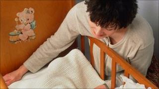 Mother putting baby in cot