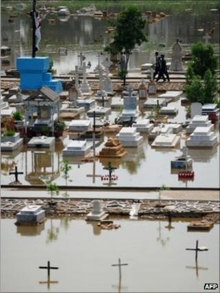 Pakistani people walk in a flooded grave yard after rain in Karachi on September 11, 2011