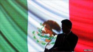 Enrique Pena Nieto, outgoing Institutional Revolutionary Party (PRI) governor in the State of Mexico, is silhouetted against the national flag before delivering his sixth and final state report in Toluca 5 September 2011