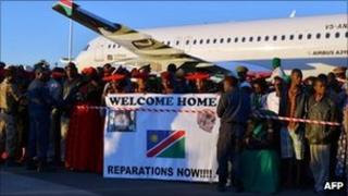 A crowd holds a banner at sunrise at the international airport in Windhoek on Tuesday, as Germany returns the skulls taken for experiments more than a century ago