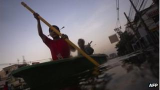 A boy and man row their boat through a flooded neighbourhood in Bangkok November 3