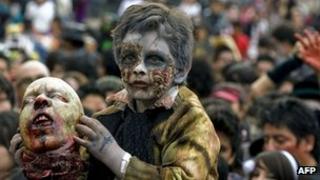 Mexican boy dressed as a zombie holding a fake severed head