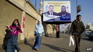 Egyptians walk past a poster for two Freedom and Justice Party candidates in Cairo (5 December 2011)