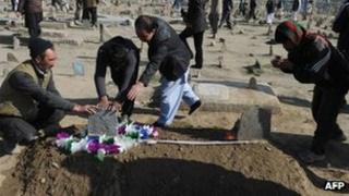 Afghan men pray over the grave of a victim of Tuesday's bomb attacks, apparently targeting Shia Muslims, at the Kart-E Sakhi cemetery in Kabul on Wednesday