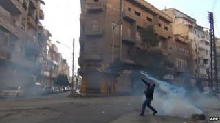 A protester throws back a tear-gas canister fired by security forces in the Syrian city of Homs (27 December 2011)