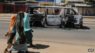 Young girls walk past a vehicle burnt on 4 November on a street of Damaturu, Yobe State, Nigeria.