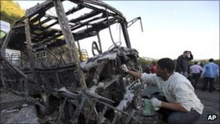 An investigator collects samples from the charred skeleton of a bus in Caracas