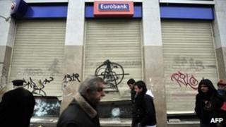 People walk past a damaged Eurobank branch in central Athens on February 13