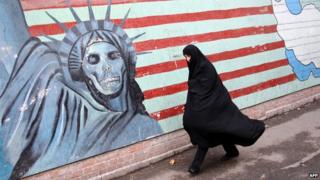 An Iranian woman walks past an anti-US mural painted on a wall