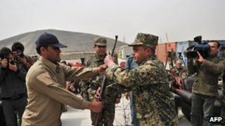 Security guard hands over a weapon to a member of Afghanistan's Public Protection Force